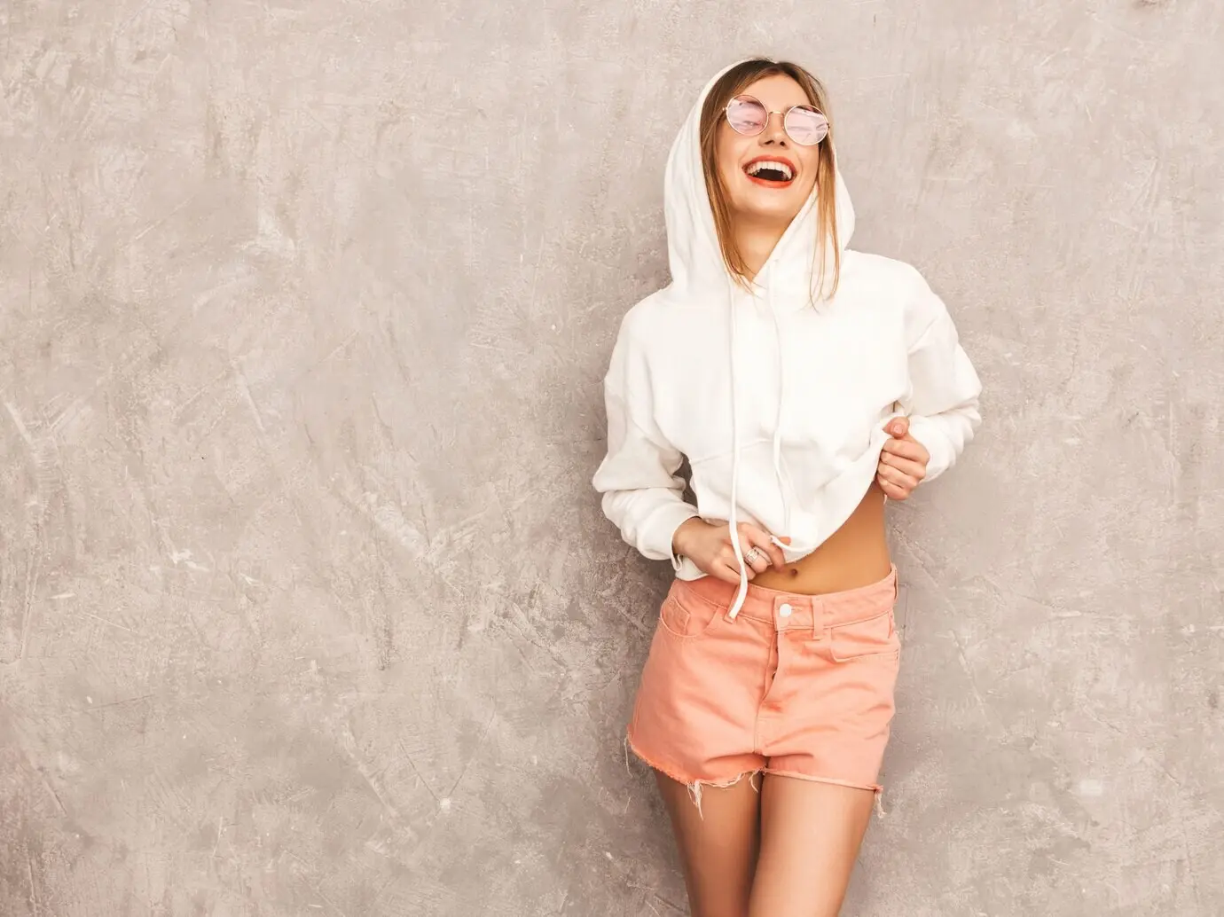 Porträt einer jungen, schönen, lächelnden Frau in trendiger sommerlicher Sportkleidung. Eine sexy, unbeschwerte Frau posiert. Ein positiv gestimmtes Model hat Spaß mit Sonnenbrille.