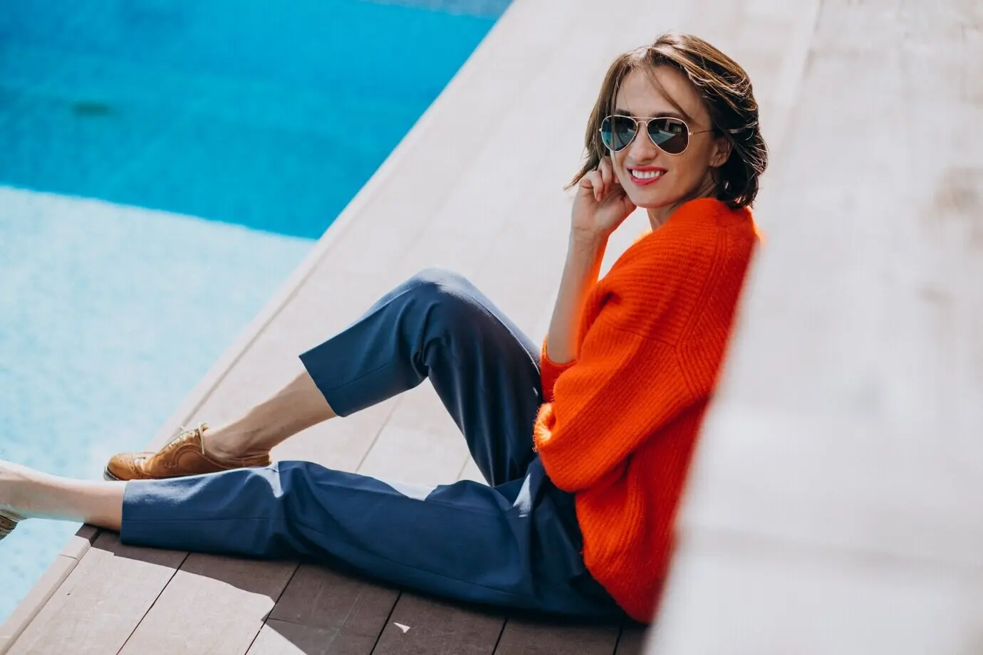 Eine attraktive Frau sitzt mit einem Telefon am Pool.